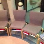Image of gray upholstered chairs with light-colored wood legs, and a small shelf to hold Bibles and hymnals underneath the seat.