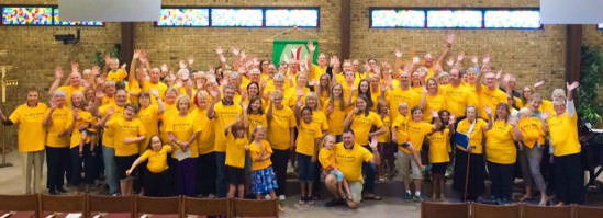 [Image description: a large group of members of Christ the Servant Lutheran Church in Allen smile and wave at the camera in their yellow "God's Work. Our Hands." Sunday t-shirts.]