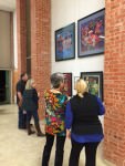 [Image description: four people, two women closer to the camera and a man and a woman further down, look at four framed works of art by Chinese artist He Qi, at the exhibit at Trinity Lutheran Church in Fort Worth.]