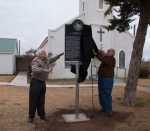 [Image description: two men unveil a historical marker in front of a church.]